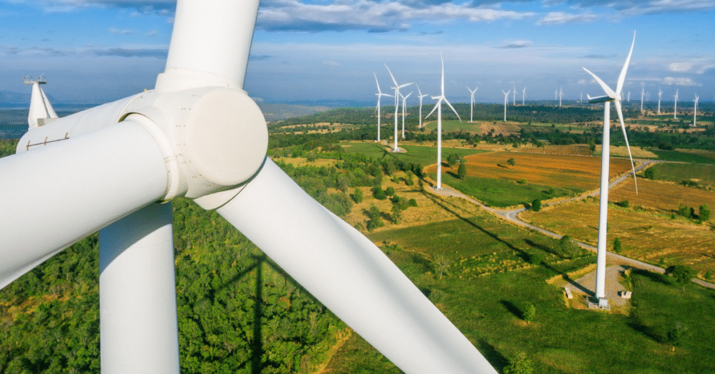 Birds eye view of wind turbine in green fields with other turbines behind it